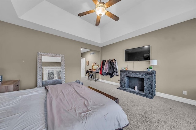 carpeted bedroom with visible vents, baseboards, a raised ceiling, and a stone fireplace