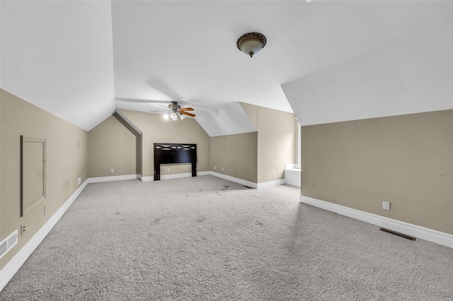 additional living space featuring light colored carpet, a ceiling fan, visible vents, vaulted ceiling, and baseboards