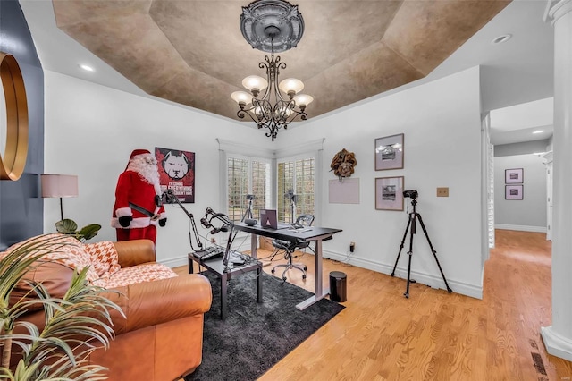 office featuring light wood-style floors, a tray ceiling, a notable chandelier, and baseboards