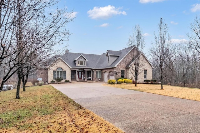 french country inspired facade with a front yard, concrete driveway, and brick siding