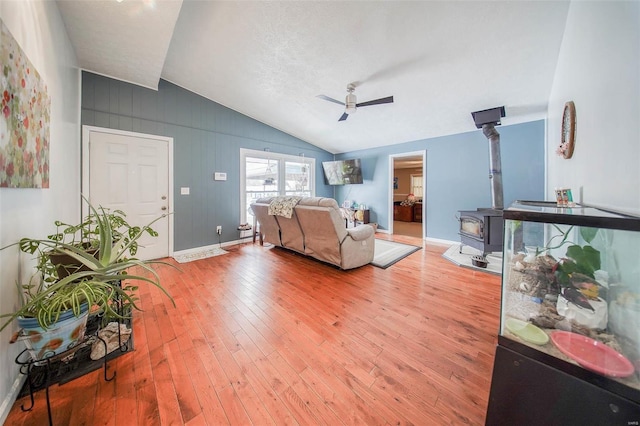 living room featuring a textured ceiling, a wood stove, lofted ceiling, ceiling fan, and wood-type flooring