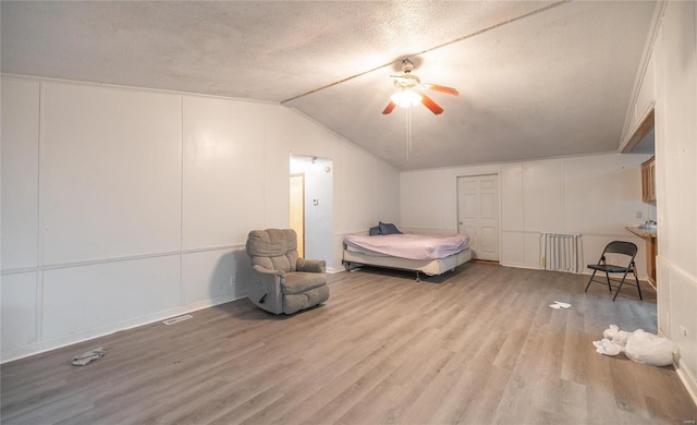 bedroom with ceiling fan, lofted ceiling, a textured ceiling, and light wood-type flooring