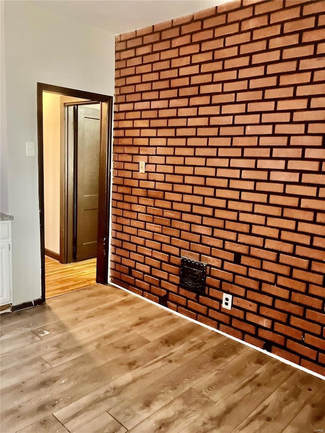 spare room featuring brick wall and light wood-type flooring