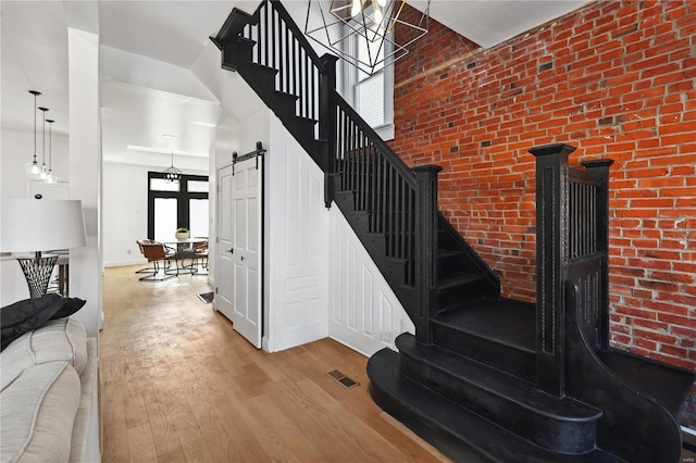 stairs with a towering ceiling, wood-type flooring, a barn door, and brick wall