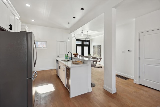 kitchen featuring pendant lighting, an island with sink, wood-type flooring, white cabinetry, and stainless steel appliances