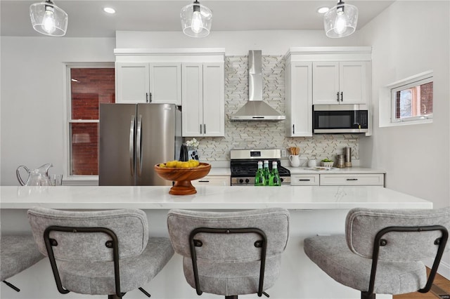 kitchen with white cabinetry, appliances with stainless steel finishes, pendant lighting, and wall chimney exhaust hood