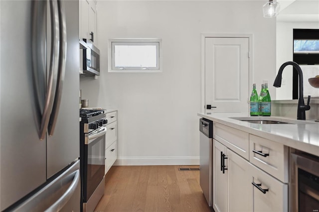 kitchen with appliances with stainless steel finishes, white cabinetry, sink, light hardwood / wood-style floors, and plenty of natural light