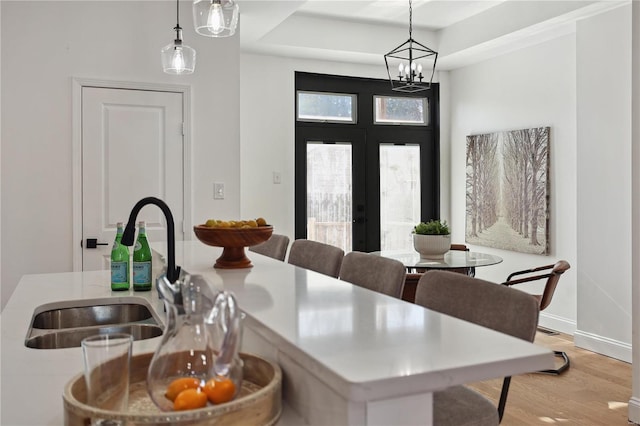 dining area with sink, a tray ceiling, light hardwood / wood-style floors, and french doors