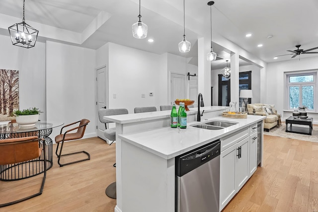 kitchen featuring sink, white cabinetry, stainless steel dishwasher, a barn door, and a kitchen island with sink