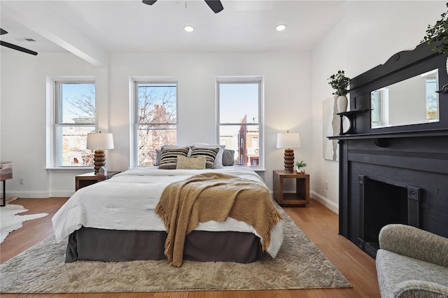 bedroom featuring a brick fireplace, light wood-type flooring, and ceiling fan