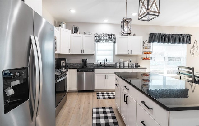 kitchen featuring white cabinets, sink, hanging light fixtures, light hardwood / wood-style flooring, and appliances with stainless steel finishes