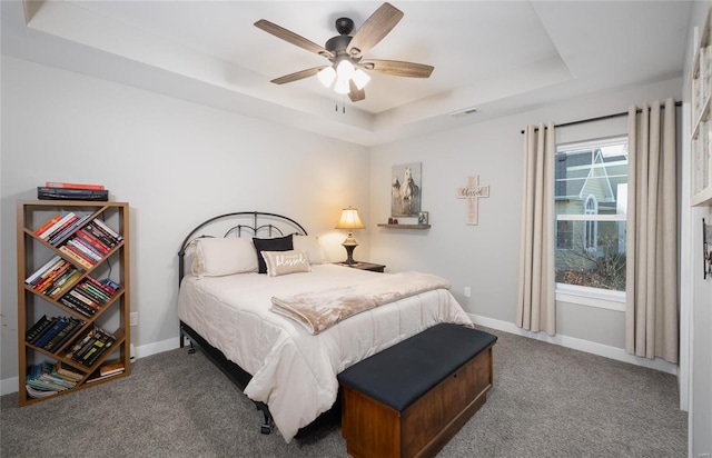 bedroom with dark colored carpet, a raised ceiling, and ceiling fan