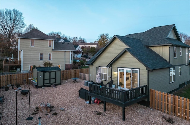 rear view of house with an outbuilding, roof with shingles, a fenced backyard, and a shed