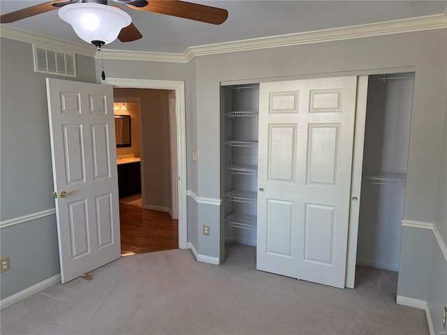 unfurnished bedroom featuring crown molding, light carpet, ceiling fan, and a closet