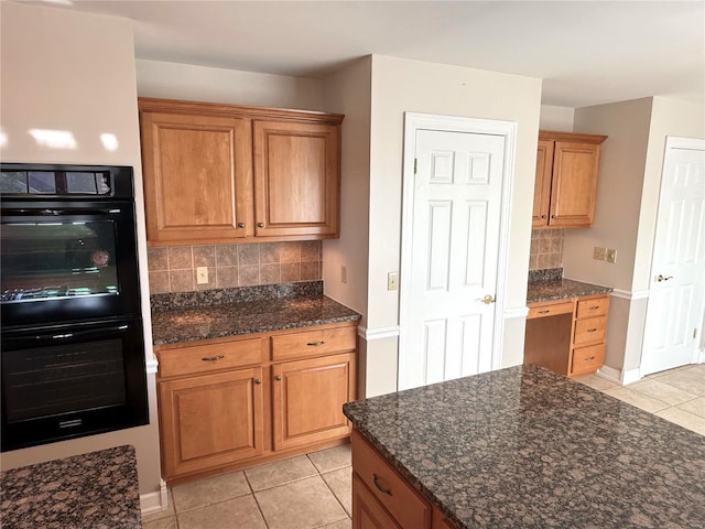 kitchen with dark stone counters, built in desk, double oven, and light tile patterned floors