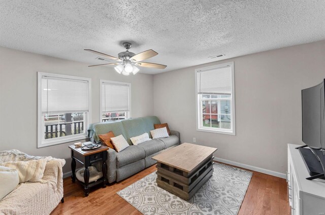 living room with a textured ceiling, light hardwood / wood-style flooring, plenty of natural light, and ceiling fan