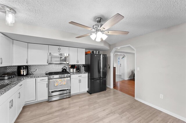 kitchen with backsplash, white cabinets, light hardwood / wood-style flooring, ceiling fan, and stainless steel appliances