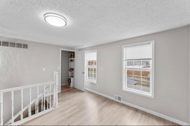 empty room with a textured ceiling, light wood-type flooring, and plenty of natural light