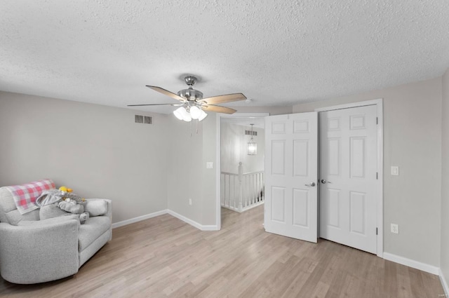 living area with a textured ceiling, light hardwood / wood-style flooring, and ceiling fan