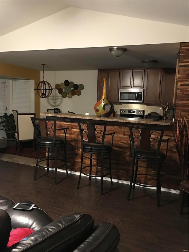 bar with stove, lofted ceiling, an inviting chandelier, dark hardwood / wood-style floors, and dark brown cabinetry