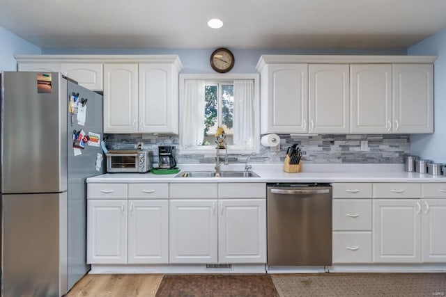 kitchen featuring appliances with stainless steel finishes, tasteful backsplash, sink, white cabinets, and light hardwood / wood-style floors