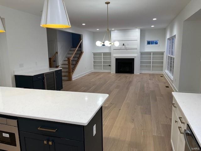 kitchen featuring a fireplace, white cabinets, pendant lighting, and light hardwood / wood-style flooring