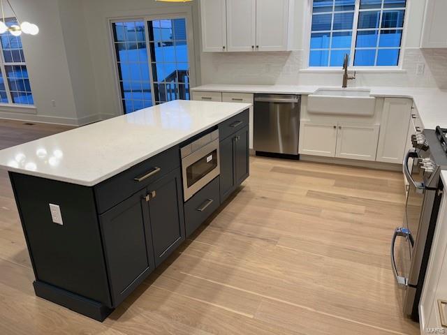 kitchen with appliances with stainless steel finishes, sink, white cabinetry, a center island, and light hardwood / wood-style floors