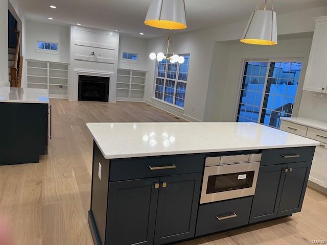 kitchen with white cabinetry, hanging light fixtures, light wood-type flooring, a kitchen island, and backsplash