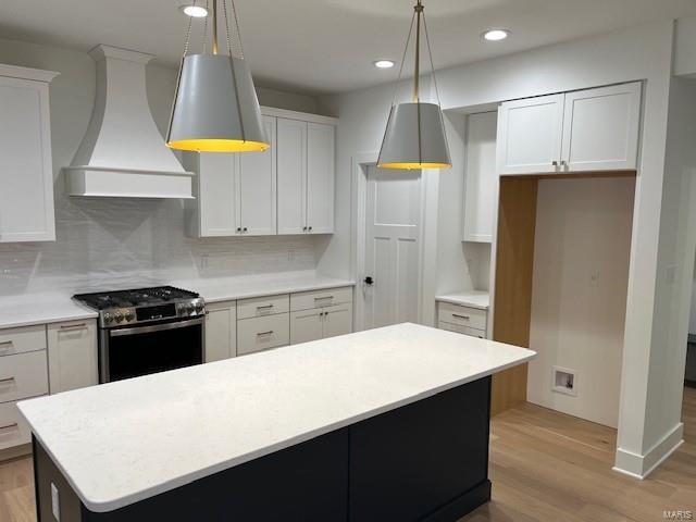 kitchen with custom exhaust hood, tasteful backsplash, white cabinetry, hanging light fixtures, and stainless steel range with gas stovetop