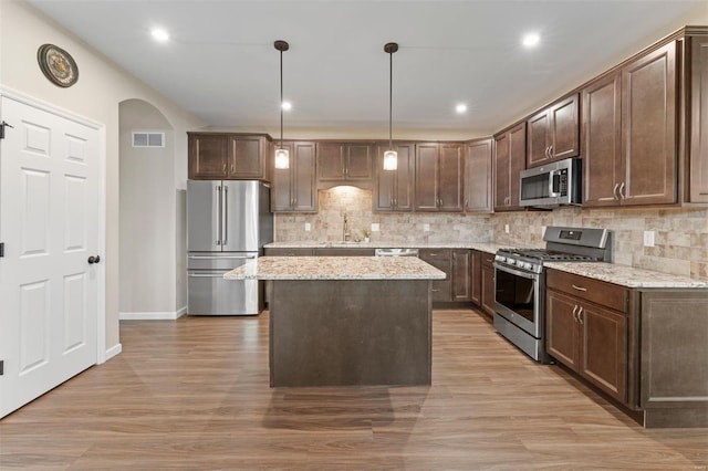 kitchen with arched walkways, dark brown cabinetry, stainless steel appliances, a sink, and backsplash