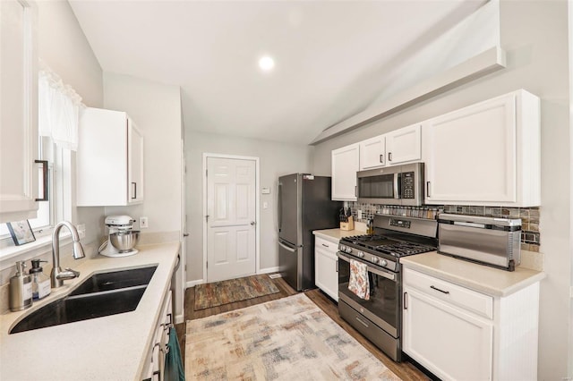 kitchen with white cabinetry, sink, vaulted ceiling, decorative backsplash, and appliances with stainless steel finishes