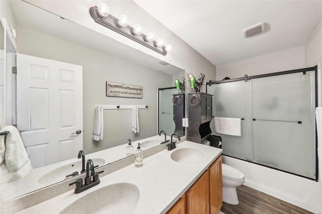 full bathroom with combined bath / shower with glass door, vanity, a textured ceiling, hardwood / wood-style floors, and toilet