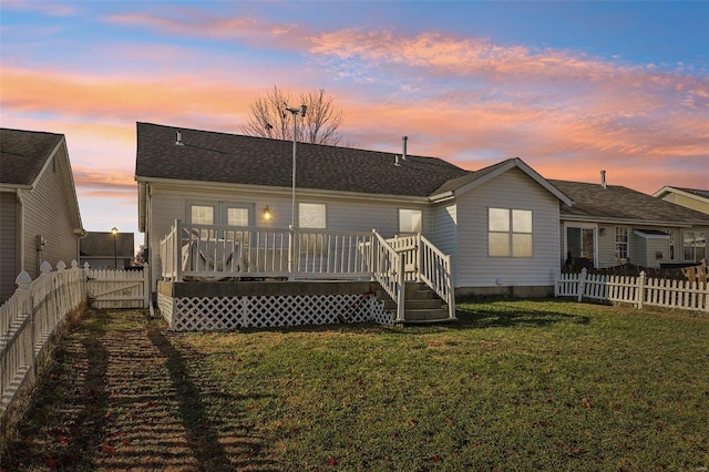 back house at dusk featuring a deck and a lawn