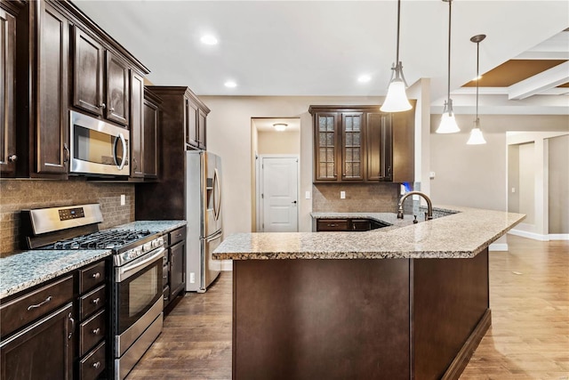 kitchen featuring dark brown cabinets, light stone counters, decorative light fixtures, and appliances with stainless steel finishes