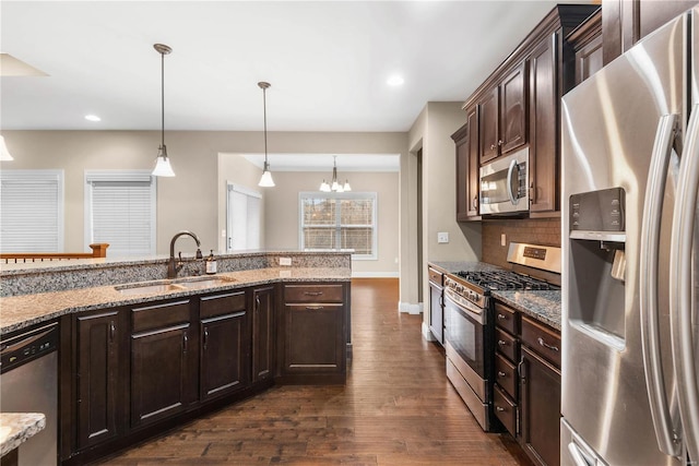 kitchen featuring light stone countertops, dark brown cabinetry, stainless steel appliances, sink, and pendant lighting