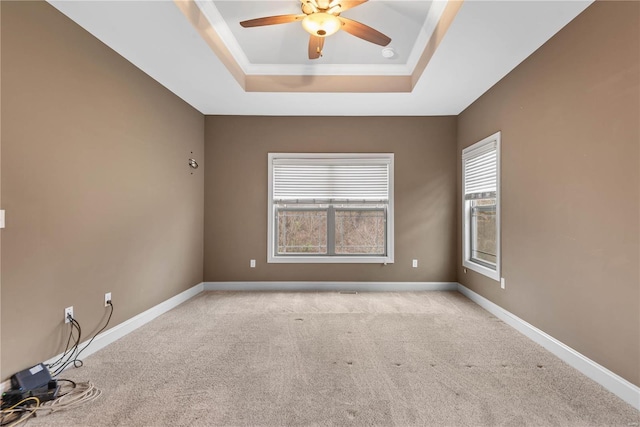 empty room with ceiling fan, a raised ceiling, light colored carpet, and ornamental molding