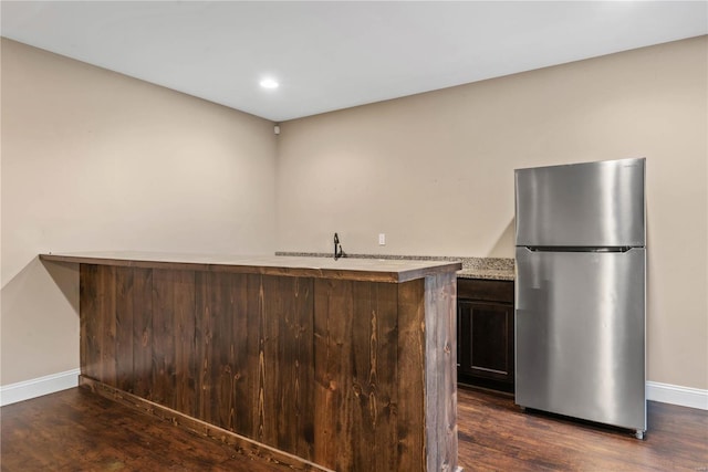 interior space with kitchen peninsula, stainless steel fridge, dark brown cabinetry, and dark hardwood / wood-style flooring