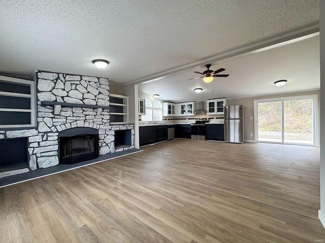 unfurnished living room with light wood-type flooring, ceiling fan, a stone fireplace, and a textured ceiling