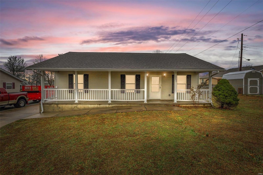 view of front of house featuring a lawn, covered porch, and a storage shed