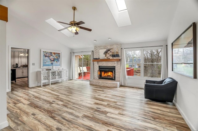 living room with wood-type flooring, a skylight, a brick fireplace, and ceiling fan