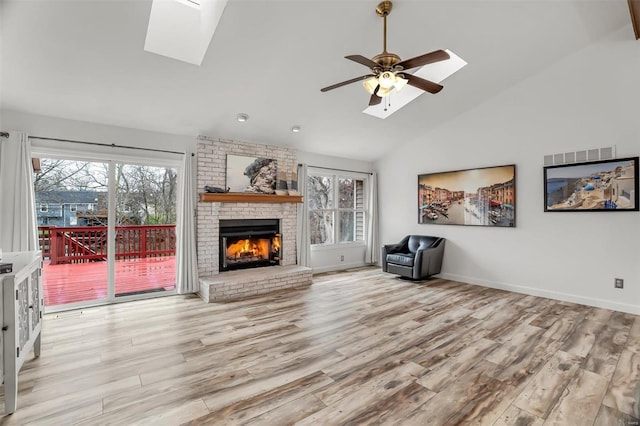 unfurnished living room featuring a brick fireplace, light hardwood / wood-style flooring, ceiling fan, and a skylight