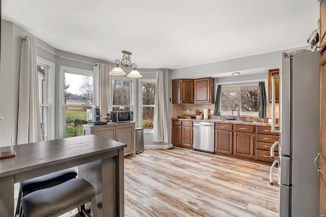 kitchen featuring appliances with stainless steel finishes, light wood-type flooring, sink, pendant lighting, and an inviting chandelier