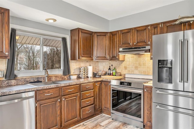 kitchen with sink, backsplash, appliances with stainless steel finishes, and light hardwood / wood-style flooring