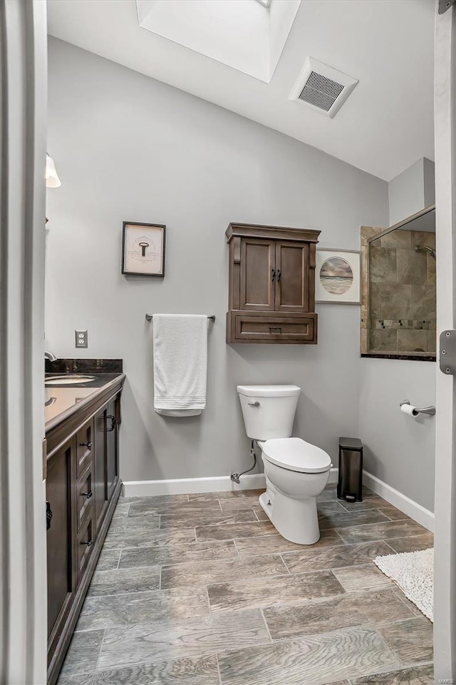 bathroom featuring vanity, lofted ceiling with skylight, walk in shower, and toilet