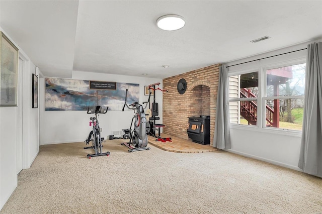 exercise room featuring carpet floors, a wood stove, and a wealth of natural light