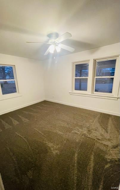 empty room featuring ceiling fan and dark carpet