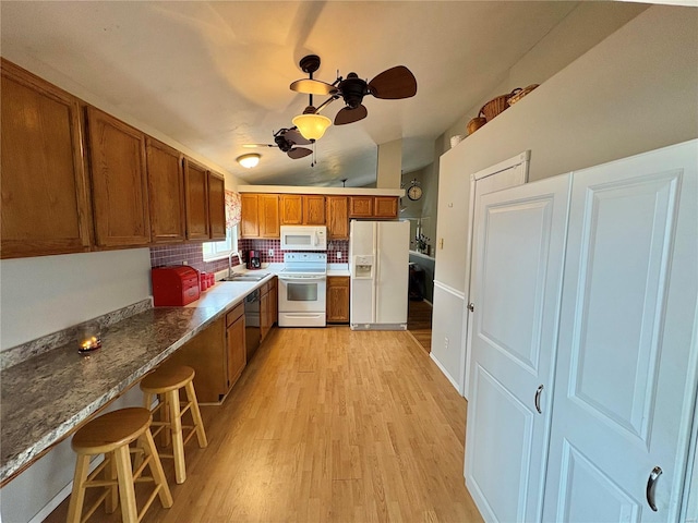 kitchen with decorative backsplash, a kitchen breakfast bar, light wood-type flooring, white appliances, and sink