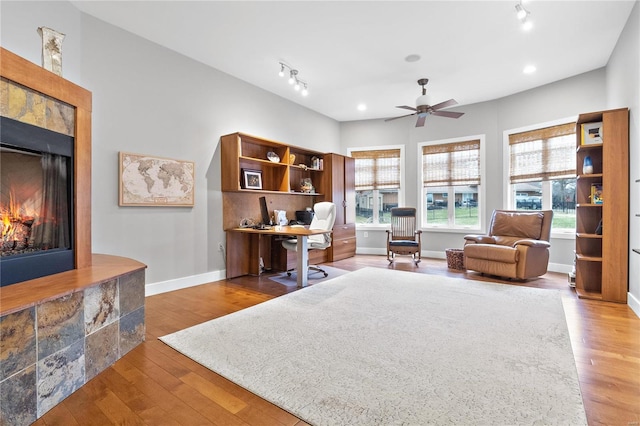 office with ceiling fan, wood-type flooring, and a tile fireplace