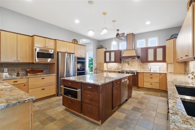 kitchen featuring light stone countertops, decorative backsplash, stainless steel appliances, decorative light fixtures, and a center island