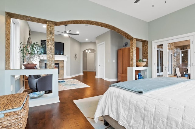 bedroom with a tiled fireplace, ceiling fan, french doors, and dark wood-type flooring